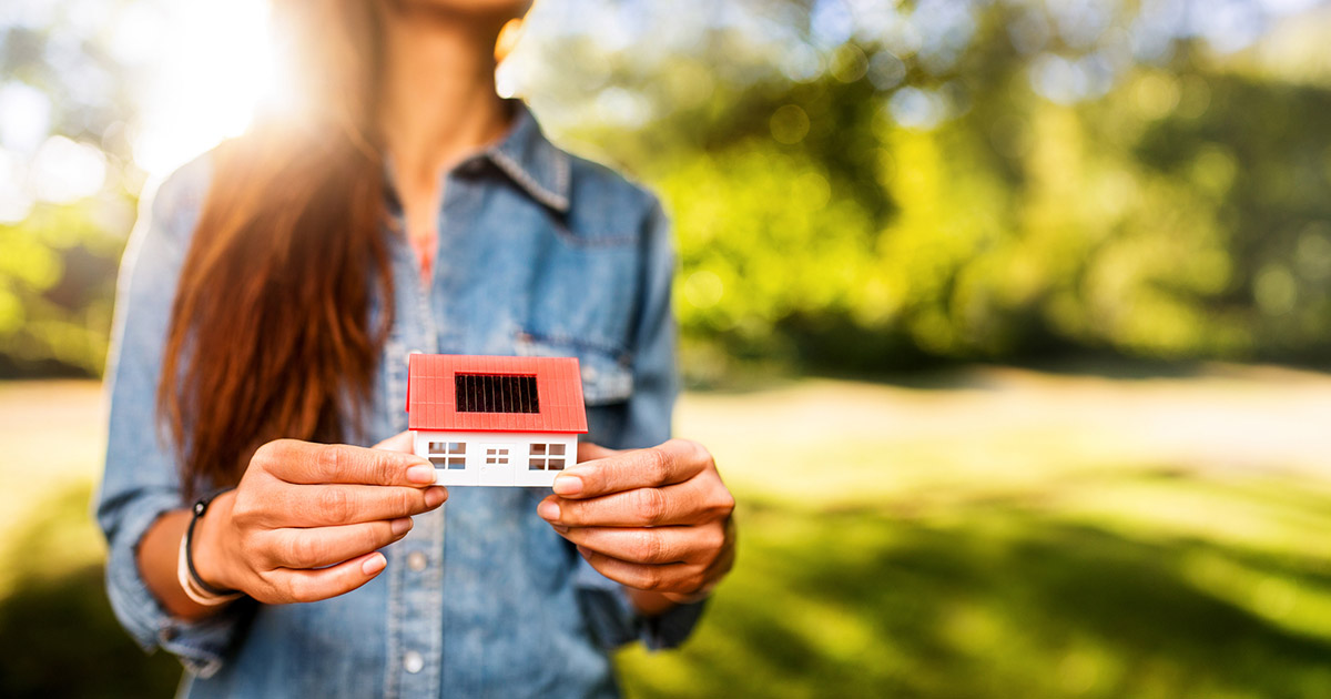 Photo of woman holding a model of a house with solar panels on it.